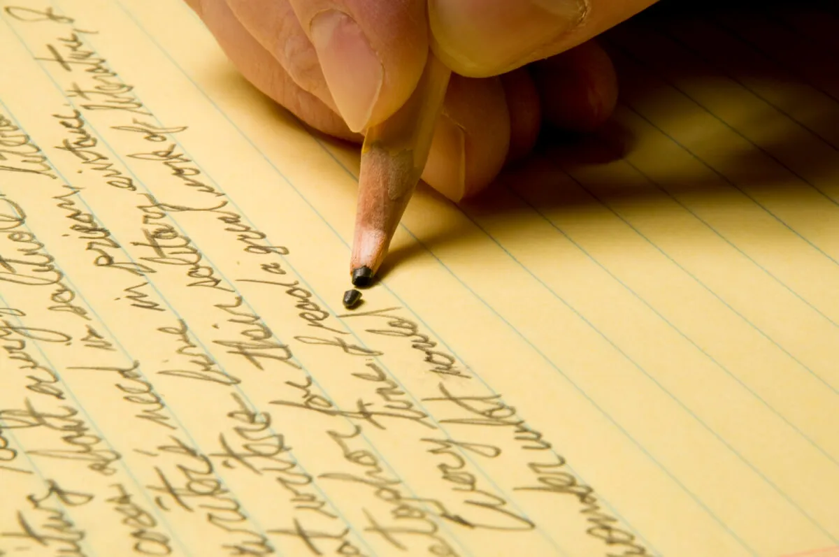 Mano escribiendo a lápiz notas apretadas en una hoja rayada amarilla, con la punta de la mina rota