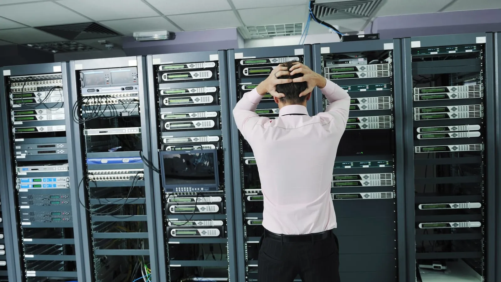 Tecnico con le mani nei capelli davanti agli armadi rack di una sala server