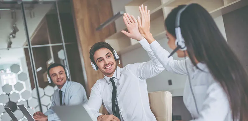 Dos agentes con auriculares chocan la mano en una oficina, con un compañero sonriente al fondo