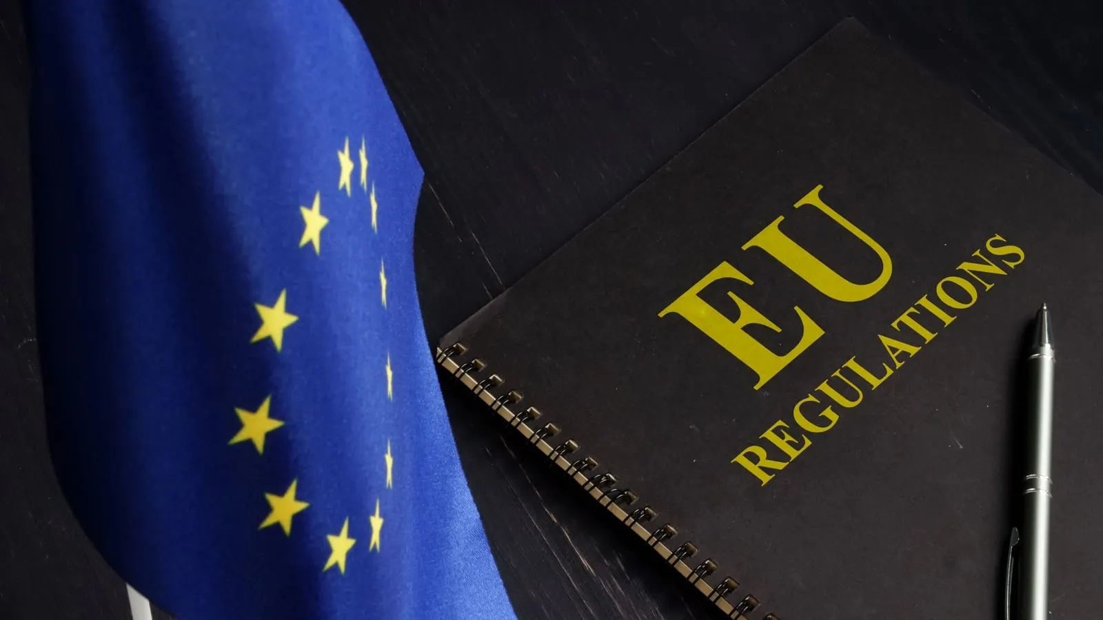 Bandiera dell’Unione Europea accanto a un quaderno con la scritta EU Regulations