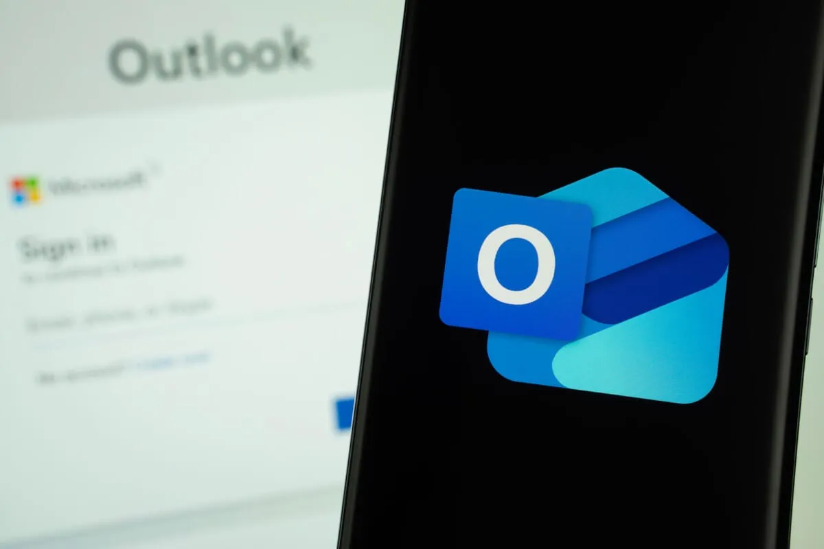 Smartphone con il logo di Outlook in primo piano e, sullo sfondo sfocato, la pagina di accesso a Microsoft